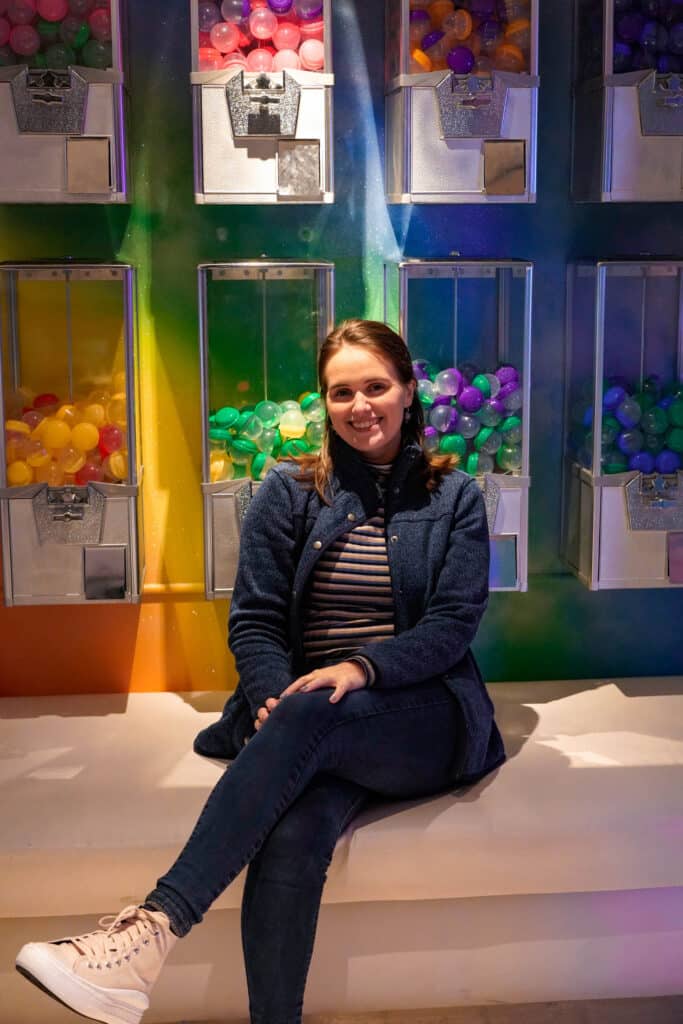 Emily sitting in front of a wall of rainbow candy and toy dispensers