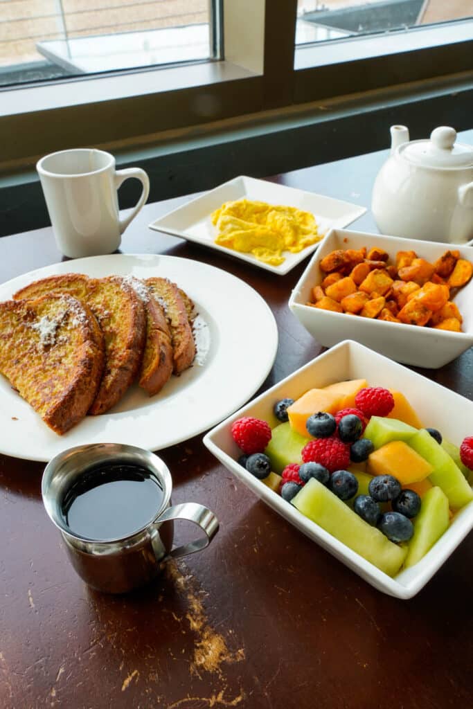 A breakfast spread of coffee, french toast, eggs, fresh fruit, and home fries.