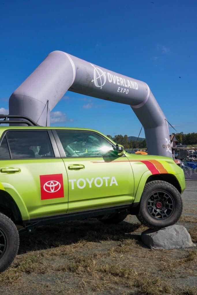 A green Toyota truck flexing on a rock in front of the Overland Expo entrance arch