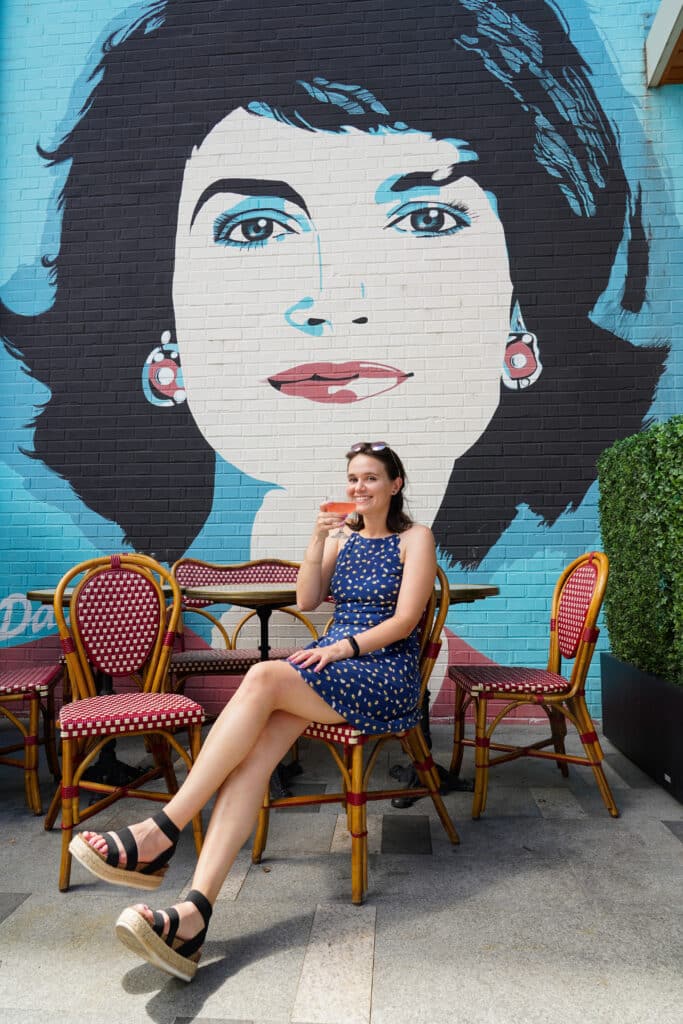 Emily sipping a drink in front of a mural