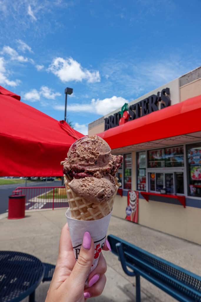 Woman's hand holding a chocolate ice cream cone in front of Bruster's Ice Cream