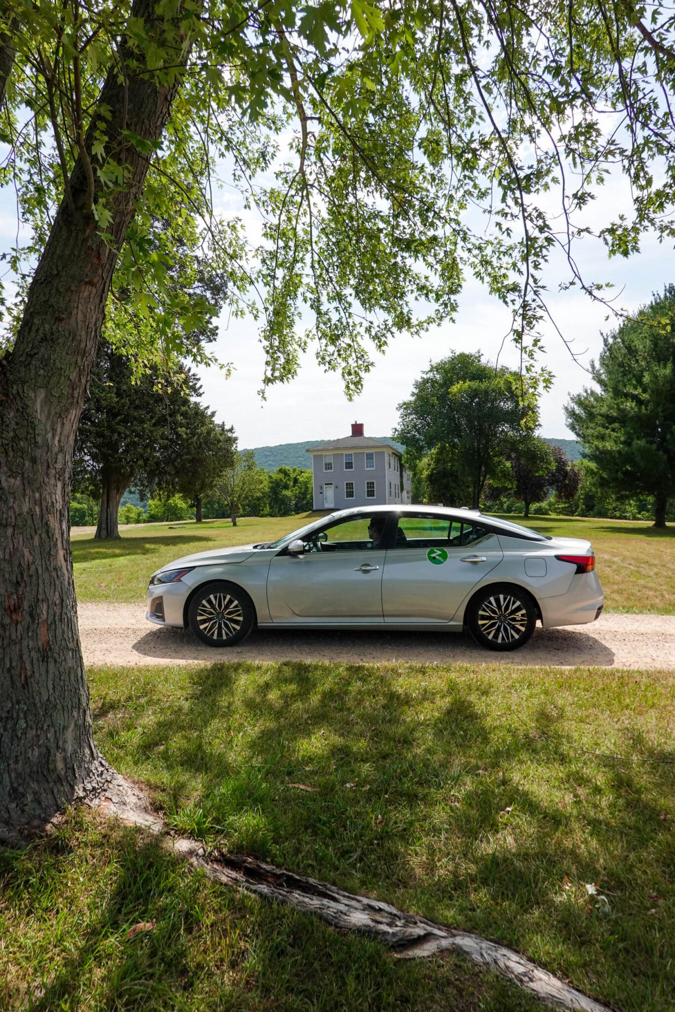 Scenic photo of a silver Zipcar sedan parked under a tree on a dirt road