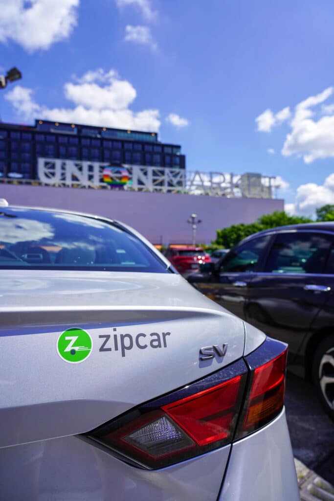 Zipcar logo on a silver sedan's bumper in front of Union Market