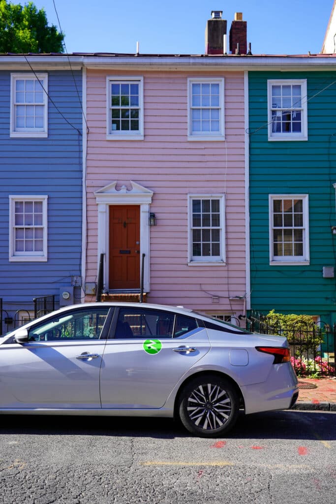 Zipcar parked in front of colorful blue, pink, and green homes